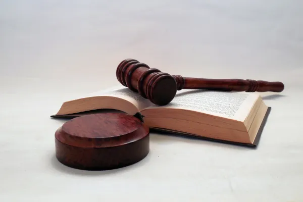 A wooden gavel resting on an open book placed on a table, set against a white background.