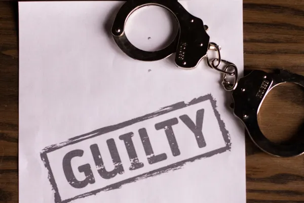 An image of a paper with the word ‘GUILTY’ printed on it and a handcuff.