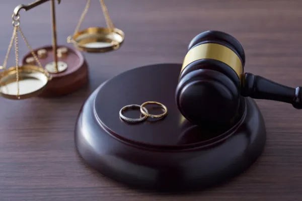 A justice scale, a wooden gavel, and a pair of rings on the table.