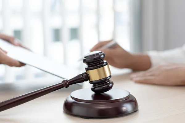 An image of a wooden gavel with a blurred background of someone signing a document.